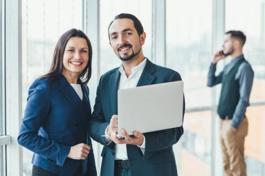 Başarılı bir iş planı yapan kadın ve erkek laptoptaki yıllık verileri karşılaştırırken, Coleague 'leri bulanık arka planda telefonla konuşuyor..