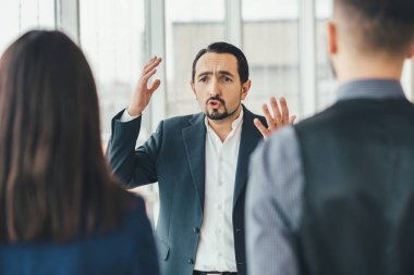 Hüsrana uğramış iş adamı umutsuzluğunu dile getiriyor, çalışanlarına bağırıyor, ellerini kaldırıyor. Kadın ve erkek ön cephede dikiliyor, bulanık..