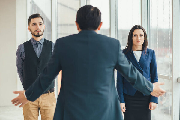 Angry boss standing back to the camera, shouting at his workers, raising hand, while stressed employees standing, with guilty look on their faces.