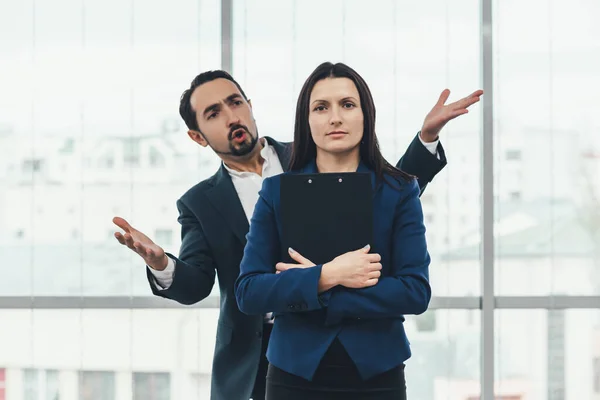 Juguetón jefe quejándose de su asistente espalda, coqueteando o burlándose, pero la mujer bonita se mantiene seria, duradera e intocable . —  Fotos de Stock