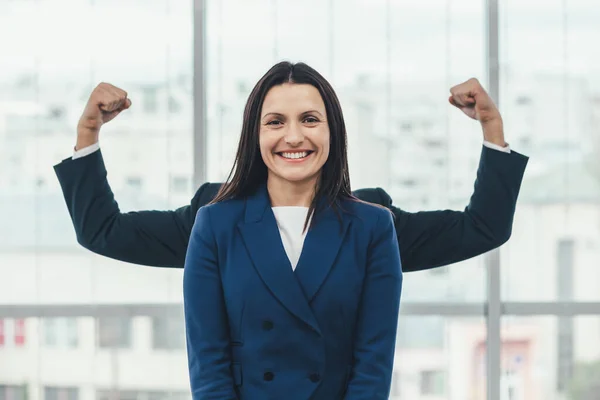 Beautiful businesswoman stands, looking at the camera smiling, while funky man plays around, standing behind her, so that only his hands raised up are seen. — Stock Photo, Image