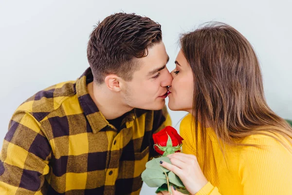 Valentines day concept. Young man and woman are kissing, girl holds a present from her boyfriend, it is a beautiful red rose.