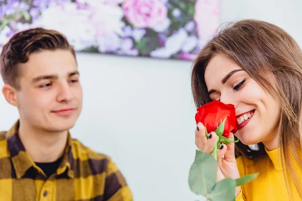 섹시 한 여자는 남자 친구가 준 장미 냄새를 맡는다. 그는 그녀가 자신의 선물을 좋아하는 것을 기쁘게 사랑으로 그녀를 쳐다 봅니다. — 스톡 사진