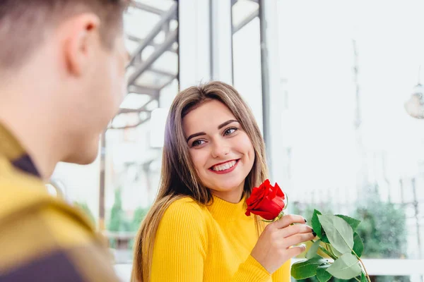 Namorado tem encontro com a namorada, dá-lhe uma grande rosa vermelha, ele sabe que as mulheres gostam de flores. Foco está na senhora irradiando com prazer, segurando uma flor . — Fotografia de Stock