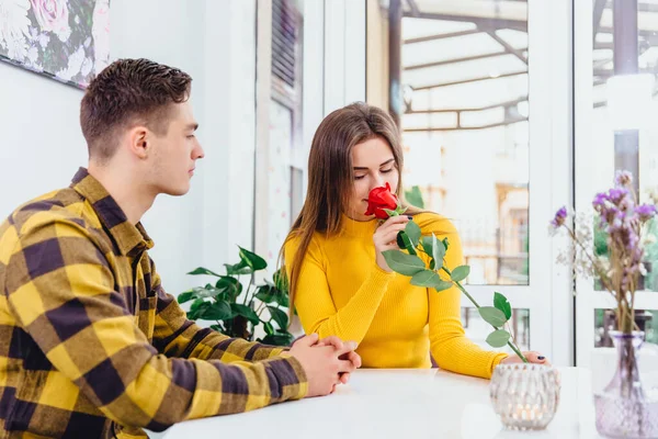 A fiatal szerelmesek a kávézóban ülve ünneplik a nászútjukat, a férfi hozott egy vörös rózsát gyönyörű fiatal nőjének.,. — Stock Fotó