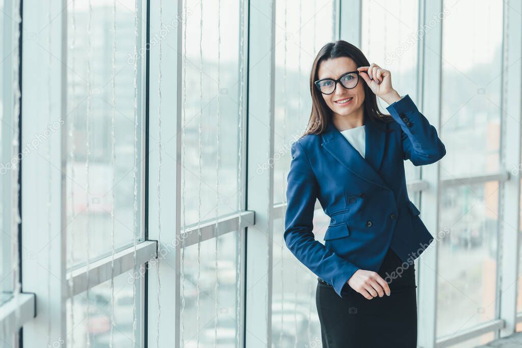 Cheerful female standing near window in her new office, expressing pleasant emotions and confidence.