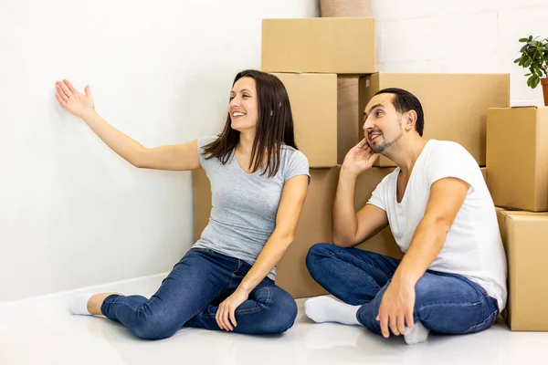 Young tired couple sitting on the floor among boxes, feeling tired but happy to move into new flat. — Stock Photo, Image