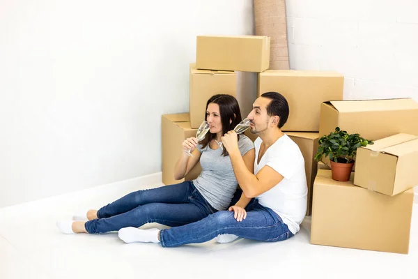 Casal jovem comemorando, sentado entre caixas, bebendo champange e plannig como eles vão fornecer sua nova casa . — Fotografia de Stock