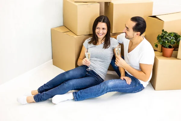 Young couple celebrating, sitting among boxes, drinking champange and plannig how they will furnish their new house. — Stock Photo, Image
