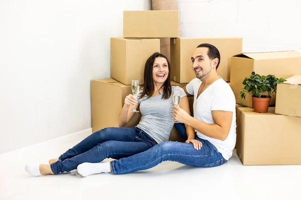 Casal jovem comemorando, sentado entre caixas, bebendo champange e plannig como eles vão fornecer sua nova casa . — Fotografia de Stock