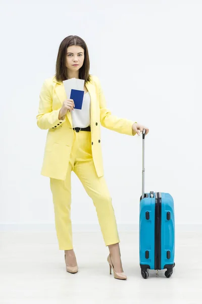 Zakenvrouw op zakenreis. Ze staat met paspoort in de hand en blauwe koffer aan haar zijde. — Stockfoto