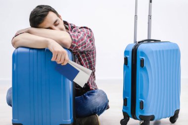 Gecikmiş uçak konsepti. Yorgun yolcu havaalanı terminalinde bavulunda uyuyor ve uçağın gelişini bekliyor..