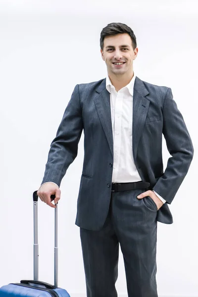 Een jonge knappe zakenman in een pak, komt met een koffer, op het station, op het vliegveld. — Stockfoto