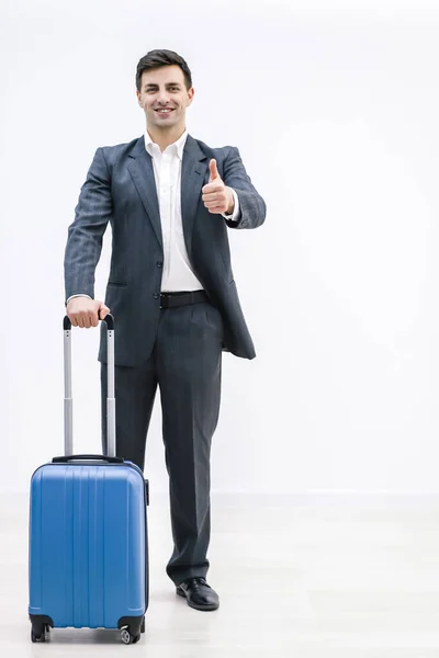 Jovem homem elegante em desgaste formal mostrando o polegar para cima, de pé com a mala do seu lado, animado para ir em nova viagem . — Fotografia de Stock