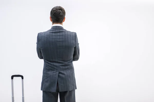 Rear view of successful businessman in suit standing in airport terminal, with suitcase over white background. — Stock Photo, Image