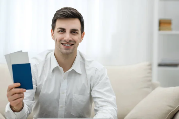 Closeup of man holding tickets for plane and passport ready for travelling, sitting on the sofa at home. — Stock Photo, Image