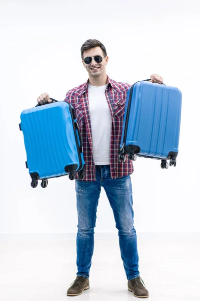 Молодий чоловік тримає дві блакитні валізи в антипапці нового місця призначення і пригод . — стокове фото