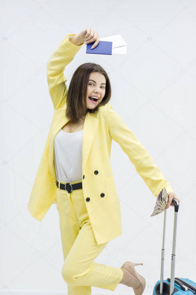 Cheerful young woman is dancing carrying a suitcase and passport, excited to go on a adventurous trip.