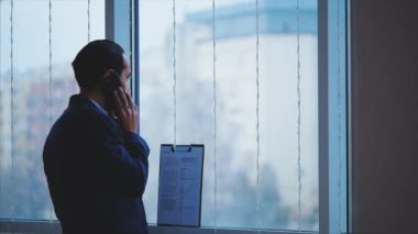 Resmi süitteki iş adamı şehir manzaralı panoramik pencerenin önünde duruyor. Ekin. Kapatın. Animasyon. 4K.