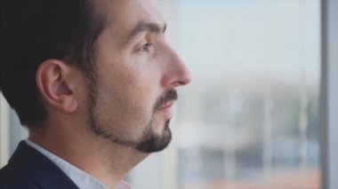 Resmi süitteki iş adamı şehir manzaralı panoramik pencerenin önünde duruyor. Ciddi bir adam. Profil görünümü. Dış profil. Kapatın. Animasyon. 4K.