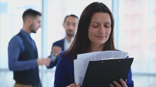 Male business workers are discussing issue on the light blurred background. Woman is turning over pages on the forefront. She is smiling. Copy space. Close up. 4K. — Stock Video