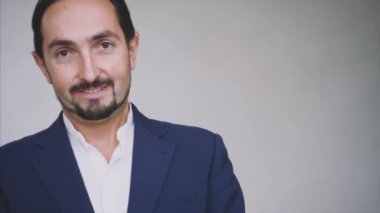 İş adamı gülümsüyor ve sallanıyor. Mavi takım elbiseli bir adam, gri arka planda izole edilmiş. Kapatın. Başla. Animasyon. 4K.