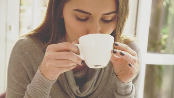 Chica joven y sttractive está en el café. Ella prueba el capuchino. De cerca. Copiar espacio. Acción. Animación. 4K . — Vídeos de Stock