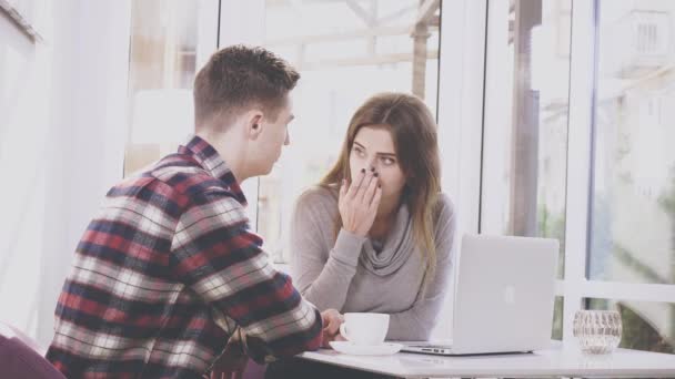 Adorable chica está sentada en la mesa en la cafetería. Ella se está comunicando con su novio, que le está mostrando algo en el ordenador portátil. Pareja concentrada. De cerca. Copiar espacio . — Vídeo de stock