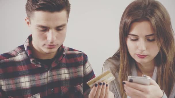 Adorable chica está sentada en la mesa en la cafetería. Se está comunicando con su novio. Chica feliz está comprando algo a través de Internet utilizando sus novios tarjetas de plástico de compras. De cerca. Copiar espacio . — Vídeos de Stock