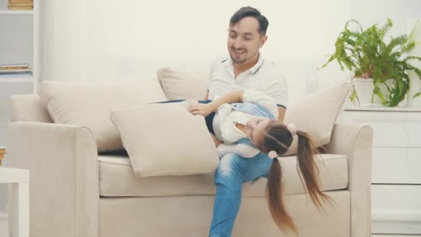 4k βίντεο βραδείας κίνησης όταν ο πατέρας παίζει με την κόρη του σε ένα λευκό καναπέ. — Αρχείο Βίντεο