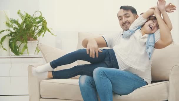 Vidéo ralenti 4k où le père joue avec sa fille sur un canapé blanc. — Video