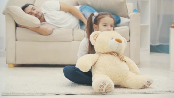 Little girl is with a teddy bear and his father is on a background in 4K slowmotion video. — Stock Video