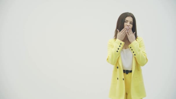 밝은 노란색 양복을 입고 하얀 배경 스튜디오에서 카메라에 공기 키스를 하는 아름다운 소녀. — 비디오