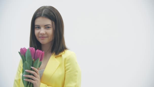 Vidéo au ralenti d'une jeune femelle sentant un bouquet de tulipes sur fond blanc. — Video