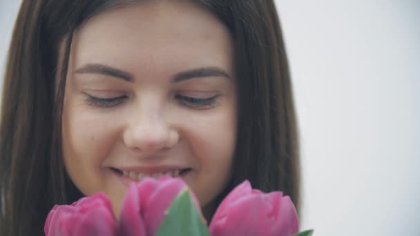 Vidéo au ralenti d'une jeune femelle sentant un bouquet de tulipes sur fond blanc. — Video