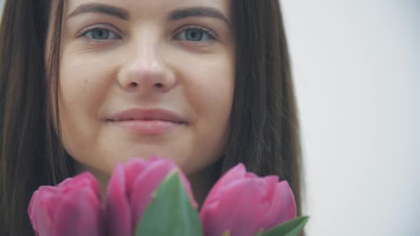 Vidéo au ralenti d'une jeune femelle sentant un bouquet de tulipes sur fond blanc. — Video