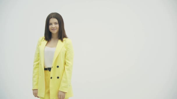 Jong schattig meisje in kleurrijke heldere slijtage buigen naar de camera en glimlachen over witte achtergrond. — Stockvideo