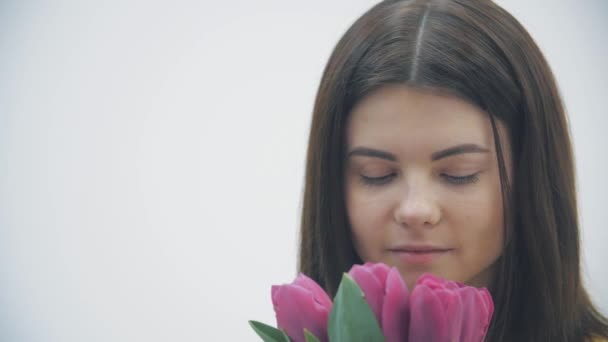 Recortado 4k video de joven hembra oliendo un ramo de tulipanes sobre fondo blanco . — Vídeos de Stock