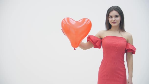 Vídeo en cámara lenta de una mujer sonriente sobre fondo blanco con globos rojos en forma de corazón en las manos . — Vídeos de Stock