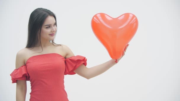 Vídeo en cámara lenta de una mujer sonriente sobre fondo blanco con globos rojos en forma de corazón en las manos . — Vídeos de Stock