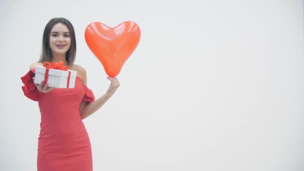 Movimento lento de mulher alegre segurando uma caixa de presente e balão de coração, sorrindo sobre um fundo branco . — Vídeo de Stock