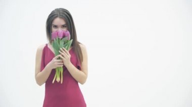 Kestane rengi elbiseli güzel bir kızın yavaş çekim videosu beyaz arka planda yumuşak laleler kokuyor..
