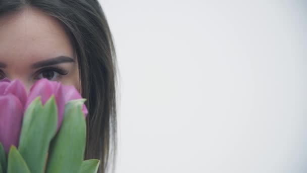 Cropped slow motion vidéo de belle fille dans la robe marron sent les tulipes tendres sur fond blanc. — Video