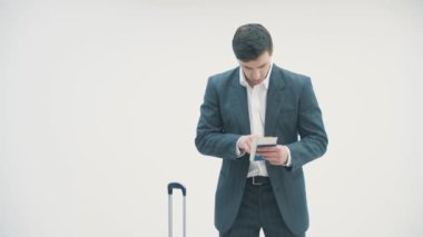 Bavuluyla meşgul bir işadamı beyaz arka planda bilet ve yatılı ekrana bakıyor..