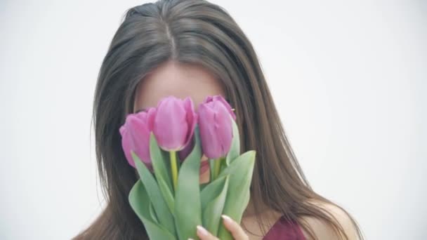 4k vídeo of young girl looking like tulip flowers she holds in hand over white background . — Vídeo de Stock