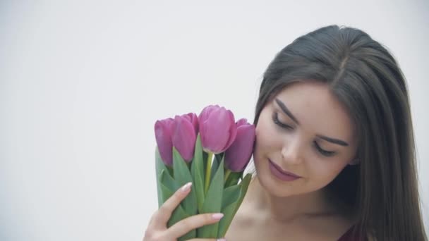 Gros plan Vidéo 4k de jeune femme mignonne sentant la tulipe rose, souriant légèrement à la caméra, regardant paisiblement. — Video