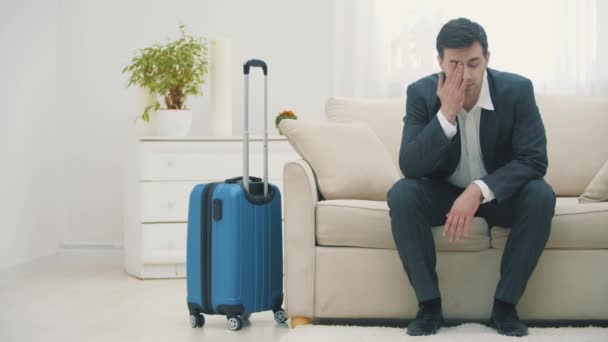 Uomo che arriva in camera d'albergo con valigia e si siede sul divano cercando molto stanco. — Video Stock