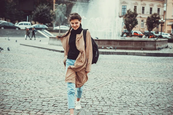 Junge Dame im trendigen Outfit läuft über den Stadtplatz, posiert lächelnd in die Kamera. — Stockfoto