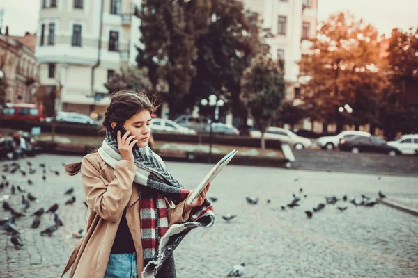 Wanita cantik turis berbicara di ponsel sambil melihat peta kota, dikelilingi oleh merpati terbang di alun-alun. — Stok Foto