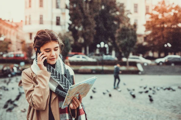 Wanita cantik turis berbicara di ponsel sambil melihat peta kota, dikelilingi oleh merpati terbang di alun-alun. — Stok Foto